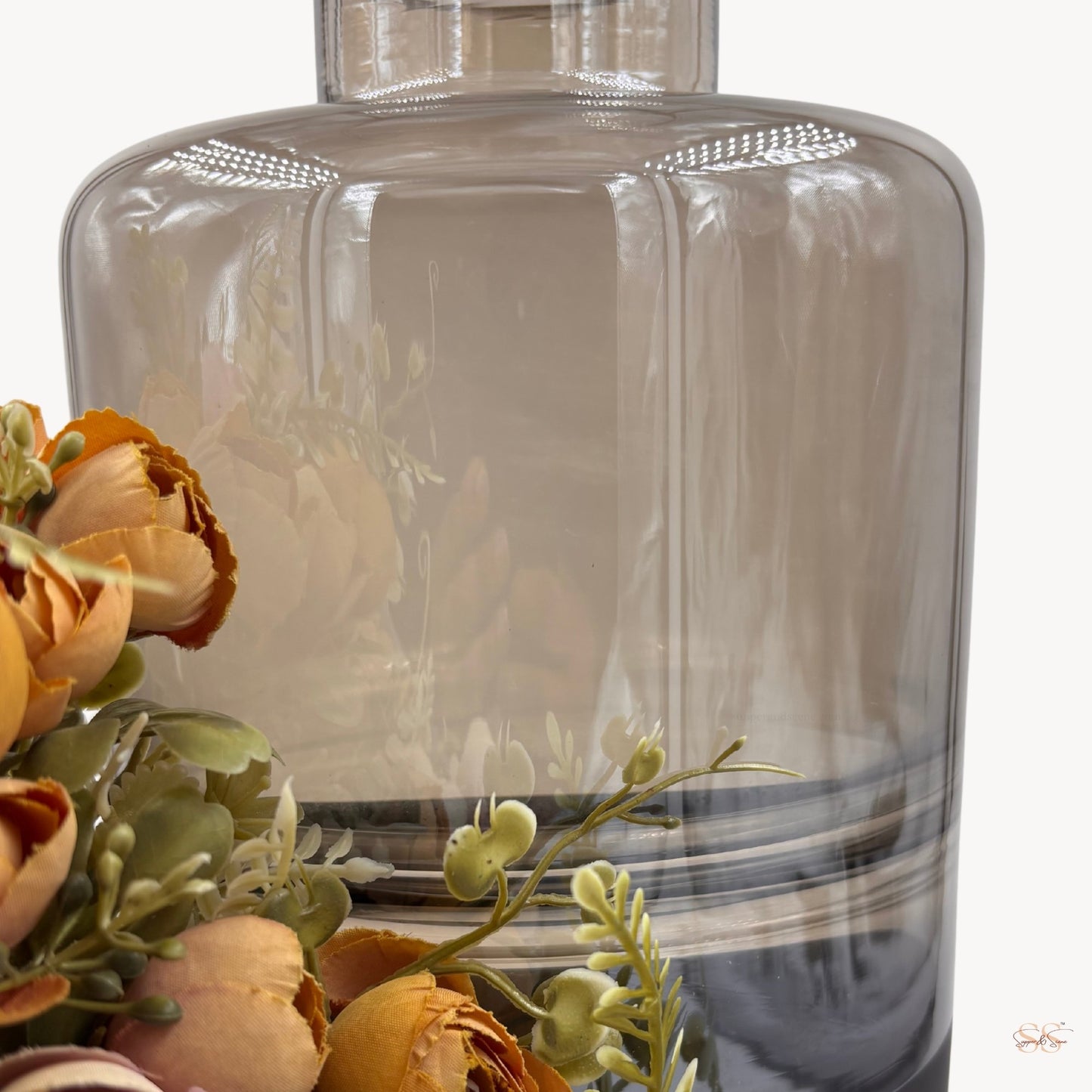Close-up of a tall smoked-glass vase with a glossy finish, showing its soft brown tint and floral arrangement beside it, by Supper and Scene.