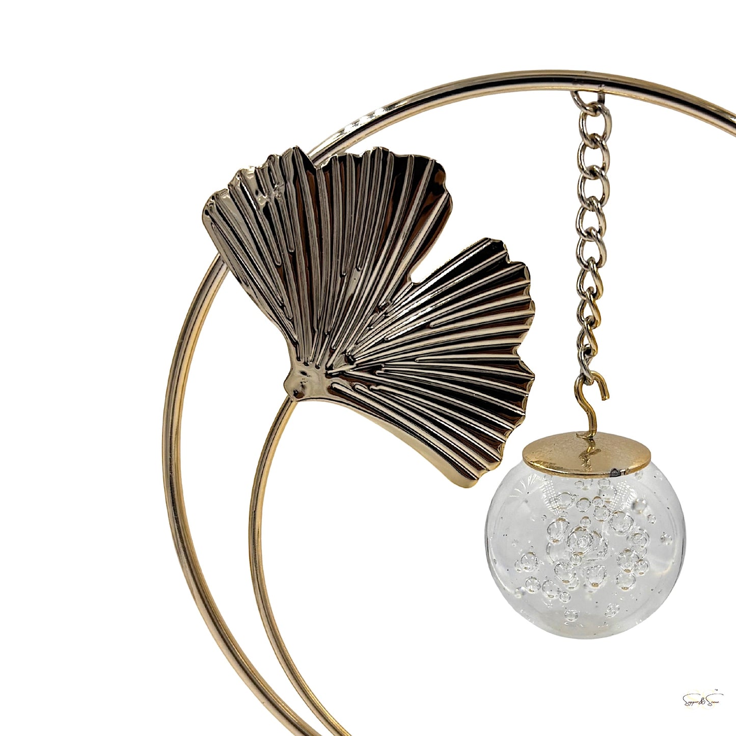 Gold metal circular showpiece with decorative leaf detailing and a suspended clear bubble-glass orb, perfect for shelf styling and centre tables, by Supper & Scene.