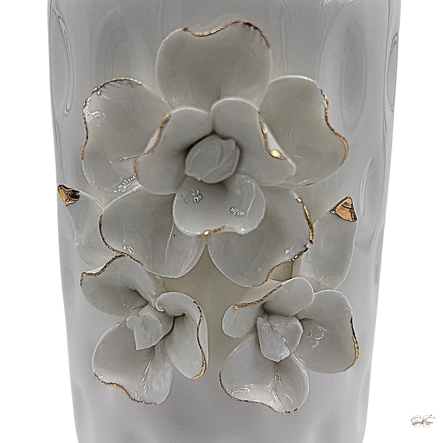 Close-up of white ceramic vase featuring raised floral motifs with gold-trimmed petals by supper and scene.