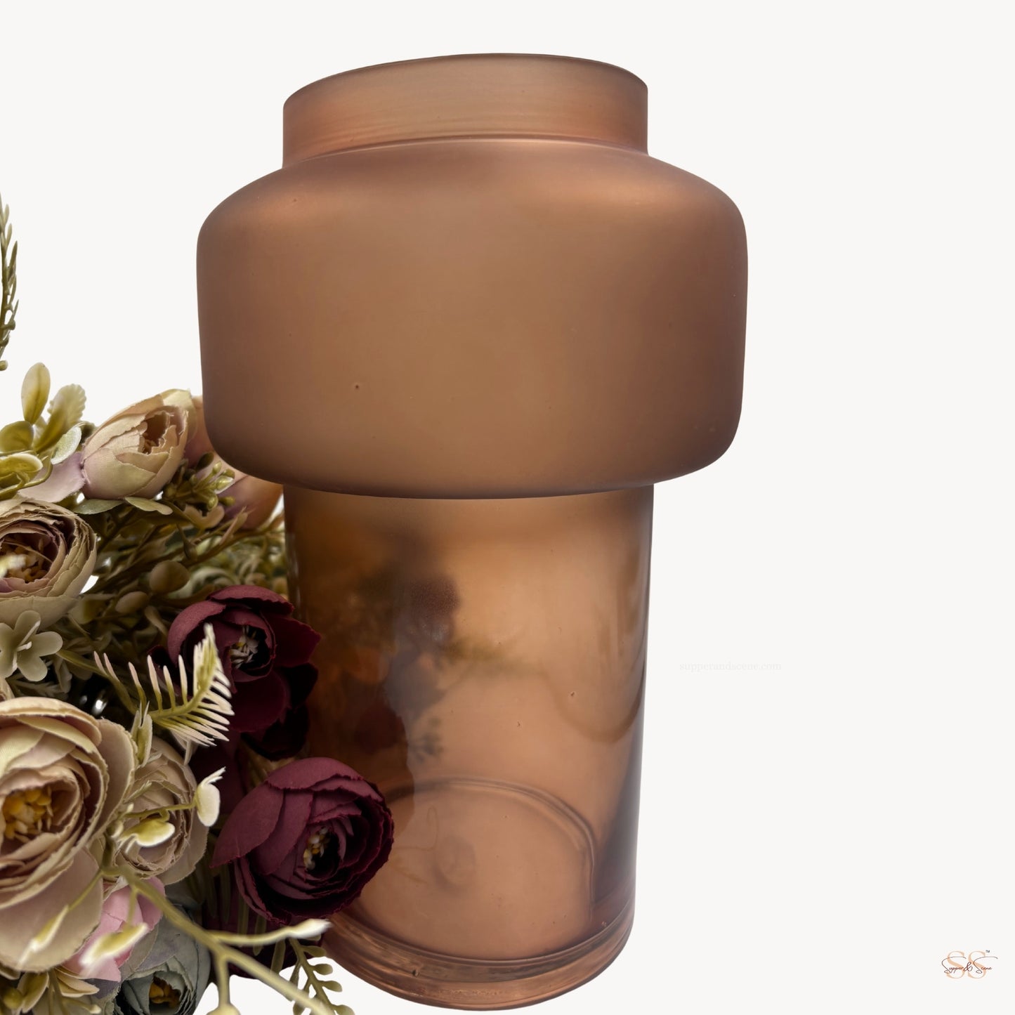 Close-up of a modern matte brown glass vase with a wide rounded top and tall cylindrical base, styled with soft pastel artificial flowers beside it, by Supper and Scene.
