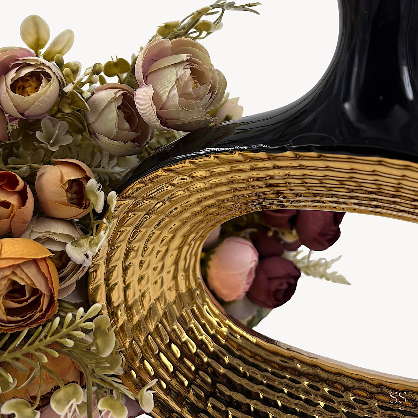 Close-up shot of a black and gold ceramic decorative vase featuring a textured oval opening, styled with artificial flowers by Supper & Scene.