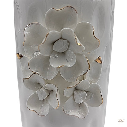 Close-up of white ceramic vase featuring raised floral motifs with gold-trimmed petals by supper and scene. 