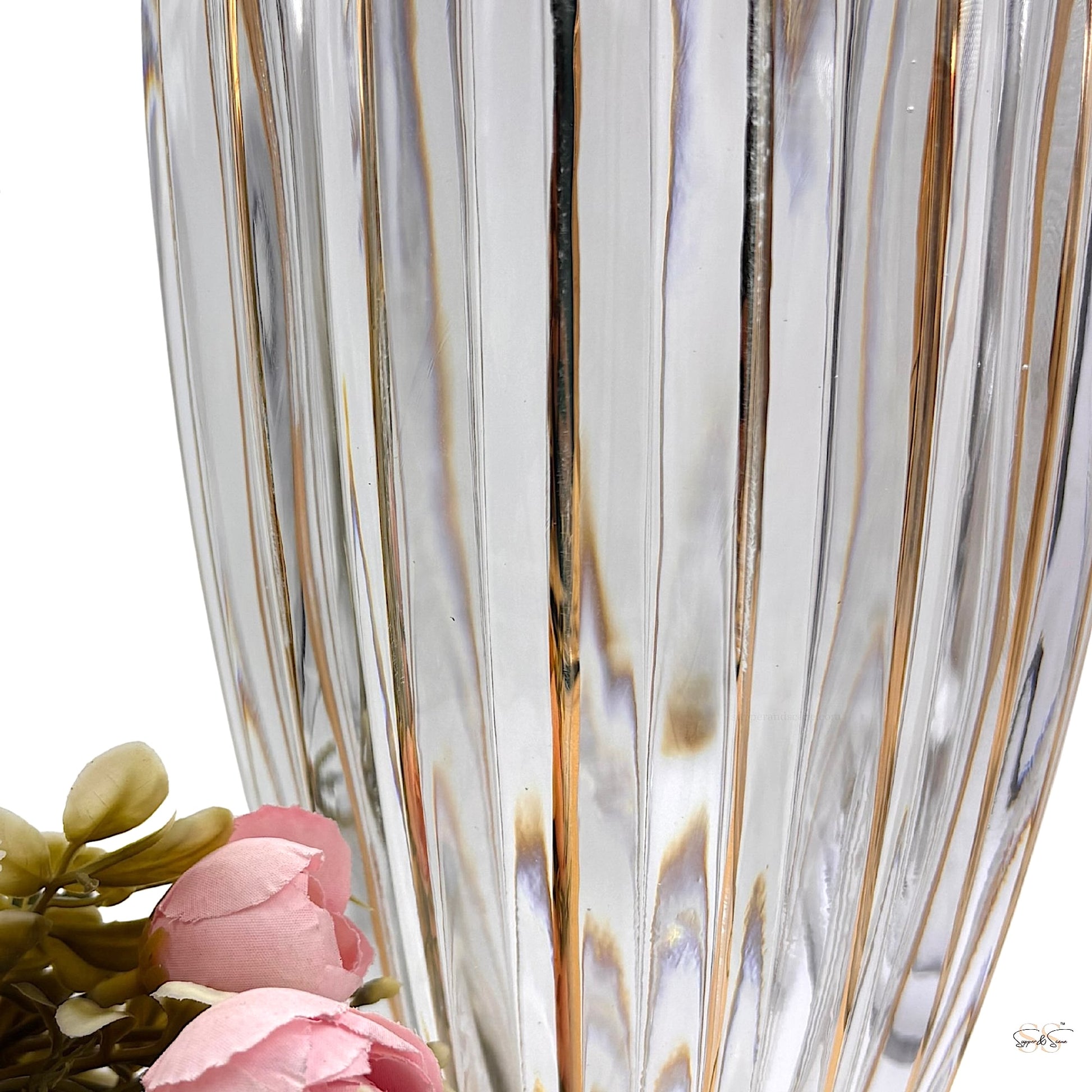 Close-up of a clear ribbed glass vase with vertical gold-accented lines, captured beside soft pink artificial flowers for an elegant styling detail by Supper & Scene.