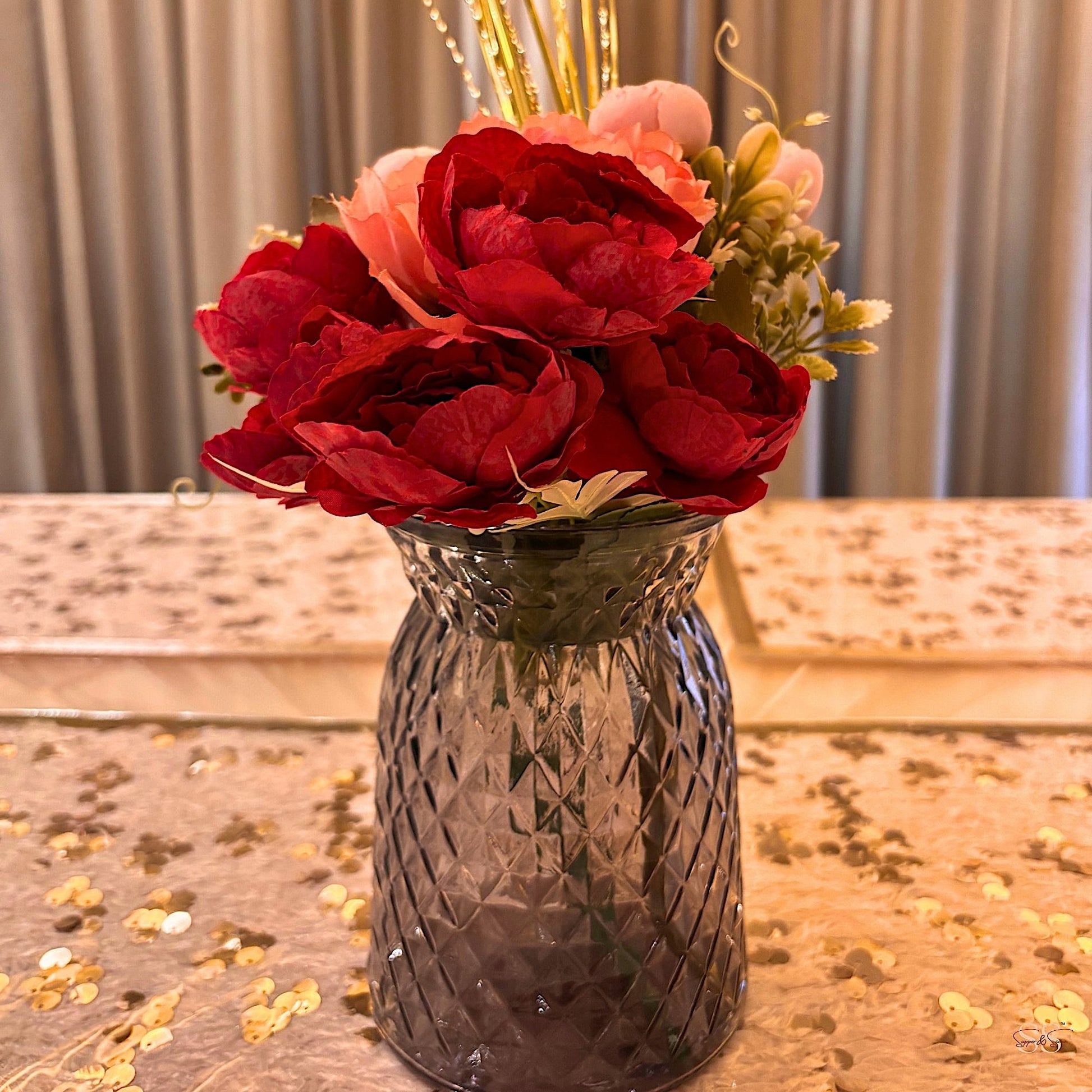 Black glass vase with red and pink artificial flowers styled on a sequin table runner by Supper & Scene