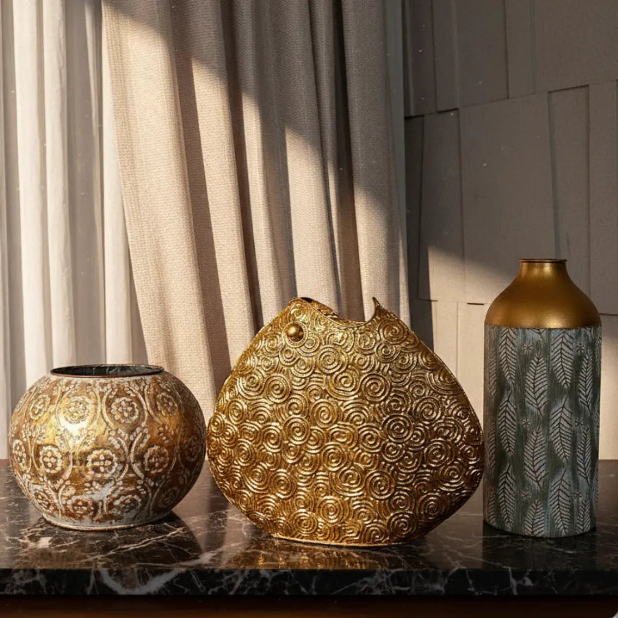 Three decorative vases on a marble surface with curtains in the background