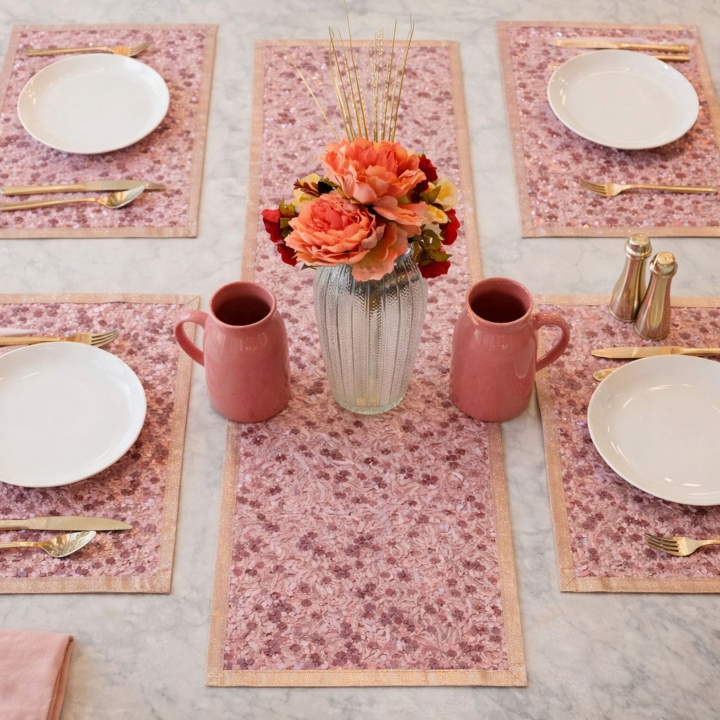 Table setting set with pink floral placemats, plates, mugs, and a vase with flowers.