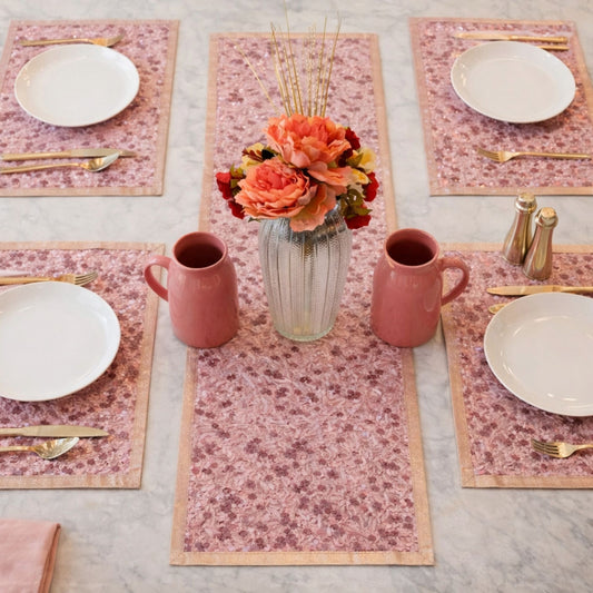 Table setting set with pink floral placemats, plates, mugs, and a vase with flowers.