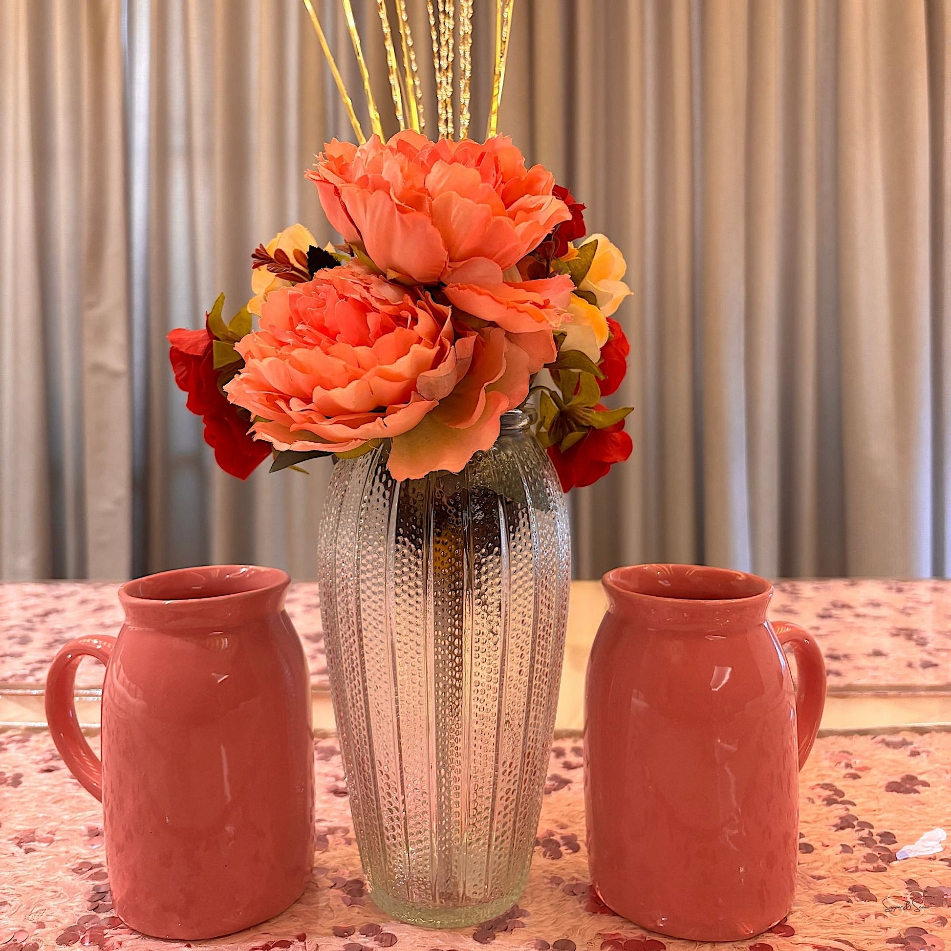 Pink sequin table décor set featuring a textured glass vase with coral flowers and two pink mugs, by Supper & Scene.