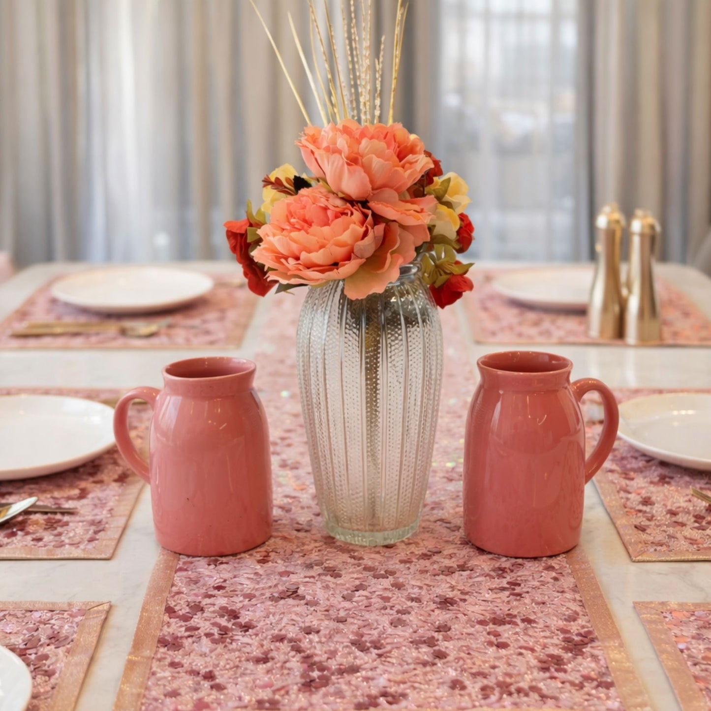 Decorative table setting with pink mugs, a vase with flowers, and patterned tablecloth.