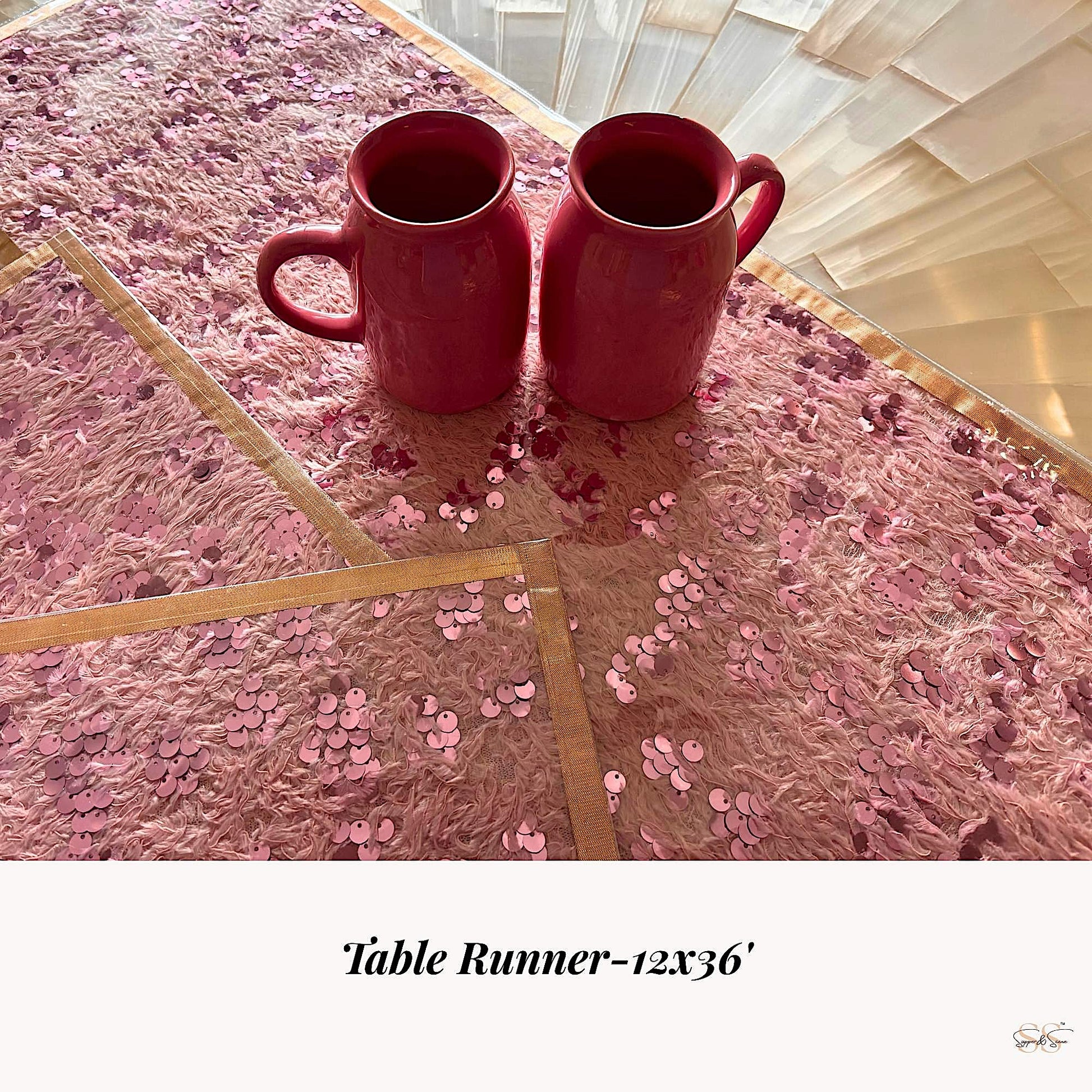 Pink sequin and faux-fur table runner with gold border styled with two pink ceramic mugs on a dining table, by Supper & Scene.