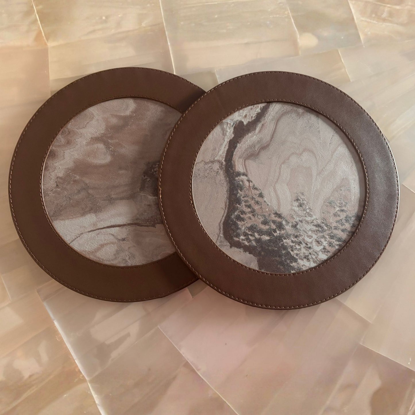 Two round marble side table mat with brown leather rims on a light stone surface.