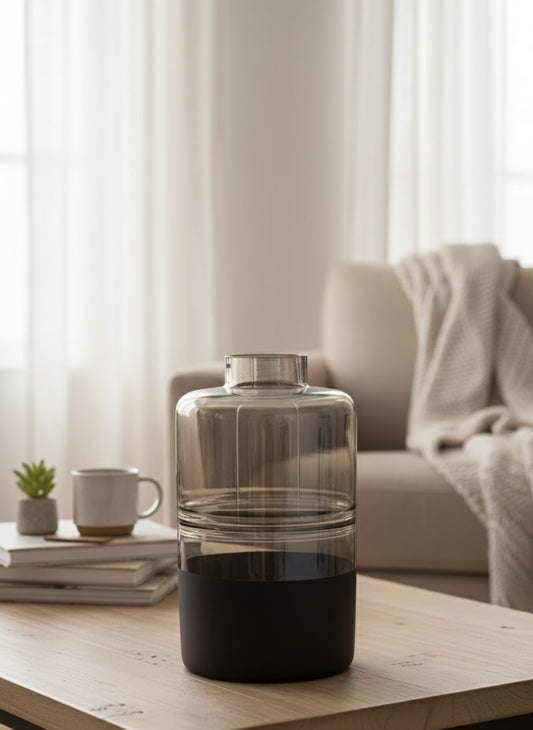 Clear glass vase with black base on a wooden table in a living room setting